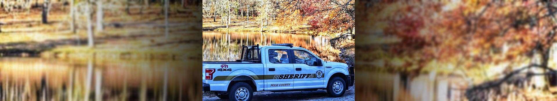 A Polk County sheriff truck parked next to a lake also featuring a backdrop of trees in the fall.