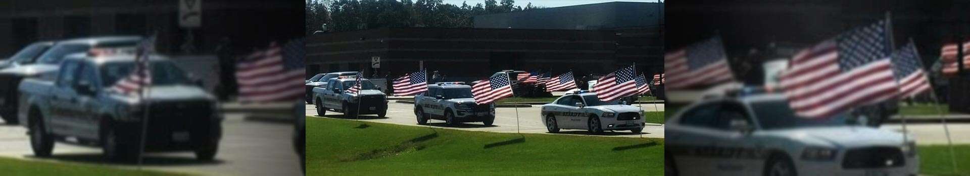 A parade of Polk County Sheriff vehicles driving next to a line of United States flags planted into the ground.
